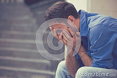 Stressed sad crying man sitting outside holding head with hands Stock Photo