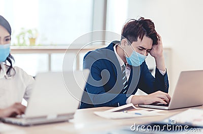 Stressed young business man wear face mask and working on laptop in office Stock Photo