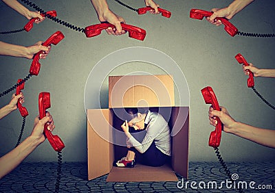 Stressed young business woman sitting hiding in a box overwhelmed by too many telephone calls and errands should be done. Stock Photo