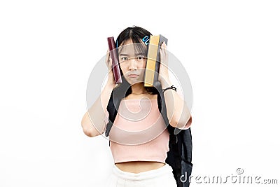 Stressful and upset Asian female college students holding pile of books with bag isolated over white background. Stock Photo