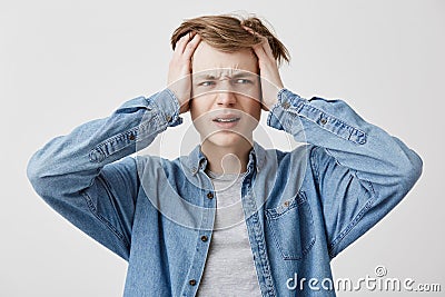 Stressful youngster with hands in fair hair has headache, clenches teeth with pain, lives in tension and has a lot of Stock Photo