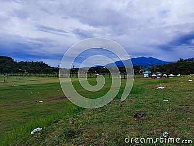 a stretch of green field with very cloudy weather Stock Photo