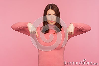 Strict bossy woman in pink sweater indicating fingers down commanding to act here and now, motivation Stock Photo