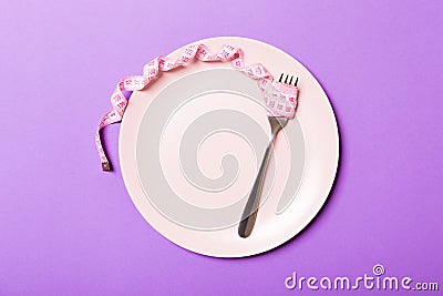 Strict diet concept with empty space fro your design. Top view of plate with fork in measuring tape on purple background Stock Photo