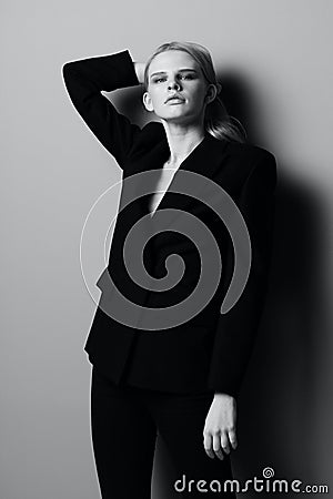 A striking blonde girl in a classic suit holds her hair with her hands and poses like a professional model in a studio Stock Photo