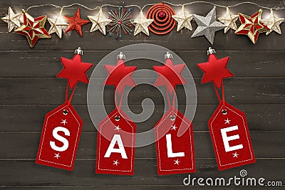 A string of golden star christmas lights, and christmas baubles, on a destressed wooden background, above hanging tags spelling Stock Photo