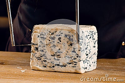 String for slicing blue cheese. Mix of cheeses on plate. Slicing dorblu, gorgonzola, roquefort. French gourmet cuisine. Stock Photo