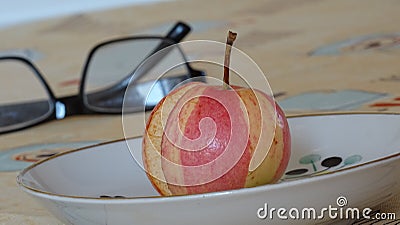 The striped apple lies in a plate on the table with a yellow tablecloth. Food. Background picture. Stock Photo