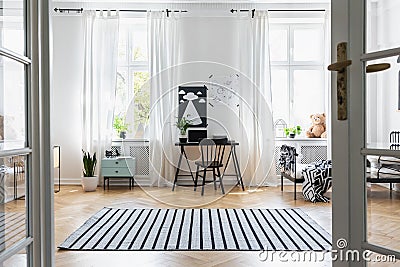 Black chair at desk in child`s room interior with windows, bed and plants. Real photo Stock Photo