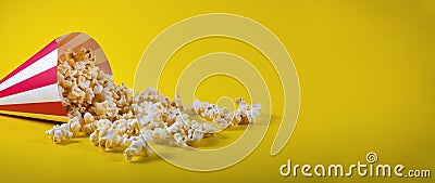 Striped cone bag with spilled popcorn on yellow background Stock Photo
