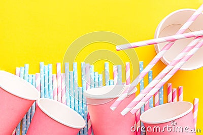 Striped pink and white blue polka dot paper drinking straws pink cups on bright yellow background. Kids birthday party celebration Stock Photo