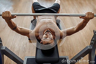 Strong athletic young man bodybuilder fitness model exercise chest with barbell on the bench in gym. Top view. Stock Photo