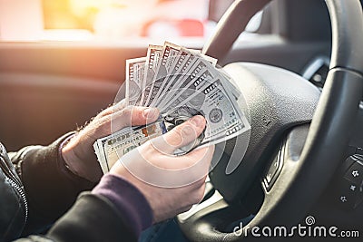 a strong bad criminal counts a large amount of dollar bills inside a car. Stock Photo