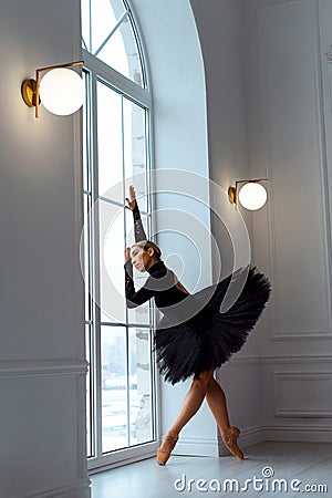 Ballerina in black tutu ballet skirt and leotard, on tiptoe in pointe shoes, near window Stock Photo