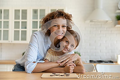 Affectionate young woman parent cuddle girl child by kitchen table Stock Photo