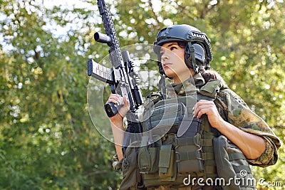 Strong brave female army soldier with rifle machine gun standing in the forest Stock Photo