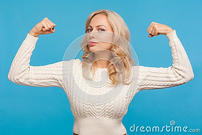 Strong independent woman with blond hair looking at camera showing her arm muscles, proud of her strength and leadership skills, Stock Photo