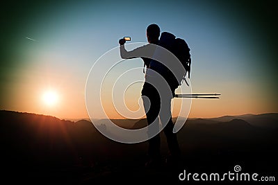 Strong man hiker taking photo with smart phone at mountain peak. Daybreak at horizon Stock Photo