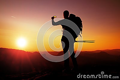 Strong man hiker taking photo with smart phone at mountain peak. Daybreak at horizon Stock Photo