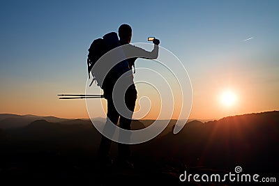 Strong man hiker taking photo with smart phone at mountain peak. Daybreak at horizon Stock Photo