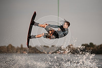 strong muscular guy jumps high and does somersault on wakeboard over the water Stock Photo