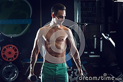 Strong Muscular man with naked torso abs working out in gym doing exercises with dumbell at biceps Stock Photo