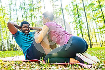 Strong and powerful afro american couple in love are working out abs exercises outside in park or forest Stock Photo