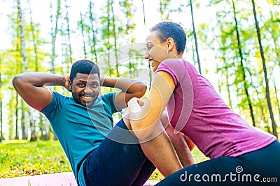 Strong and powerful afro american couple in love are working out abs exercises outside in park or forest Stock Photo