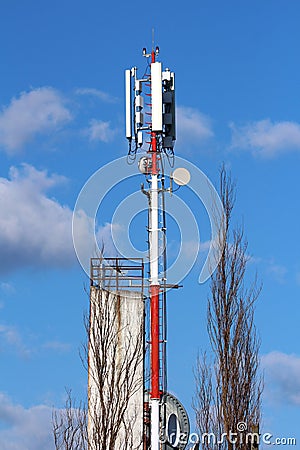 Strong red and white metal pole with various shapes and sizes cell phone transmitters and antennas next to tall building and Stock Photo