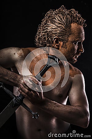 Strong warrior licking a sword, covered in mud and naked Stock Photo
