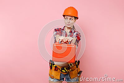 Strong young handyman woman in orange helmet, plaid shirt, denim shorts, kit tools belt full of instruments, toolbox Stock Photo