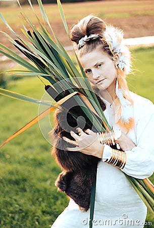 Strong young woman with a bulrush grass reed on rural field background at sunset Stock Photo