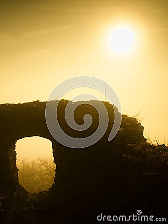 The stronghold. Stony ruin of medieval stronghold tower on hill. Early morning sunshine hidden in heavy autumn mist. Stock Photo