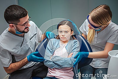 Stubborn girl sit in ddental cair in room. Dentists look at her worried. They touch and talk to her. on green Stock Photo