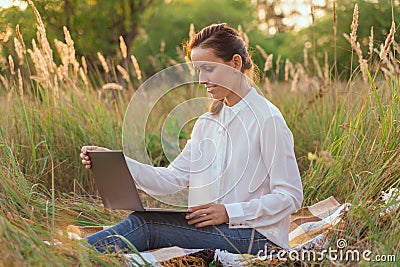A student does homework online sitting on the beach in a field Stock Photo