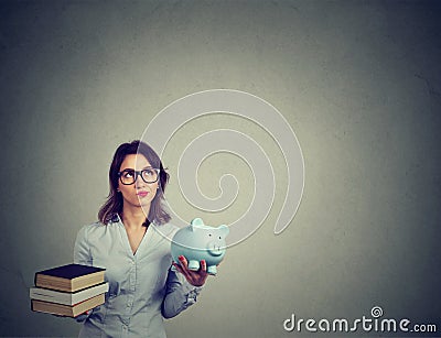 Student loan concept. Woman with pile of books and piggy bank full of debt rethinking future career path Stock Photo