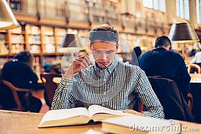 Student man sitting on the desk in library reading room and doing research reading books Stock Photo