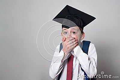 Student scared covered his mouth with his hands. Boy in school uniform and academic hat. White background Stock Photo