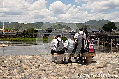 Student schoolchildren are sitting on a bench near Katsura river, Kyoto, Japan Editorial Stock Photo