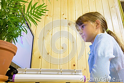 The student sits at the table in front of the monitor and carefully reads the task Stock Photo