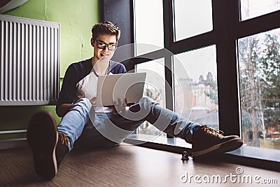 Student working with laptop sits on the floor near the window Stock Photo