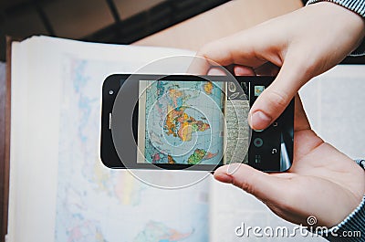 Student young woman taking a photo world map image book on screen black with Smartphone. Top view. Female hand holding and touch Stock Photo