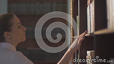 Studente di college femminile che cattura libro dalla mensola in libreria mano del cavo sugli scaffali con i libri stock footage Studente di college femminile che cattura libro dalla mensola in libreria mano del cavo sugli scaffali con i libri stock footage
