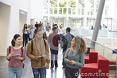 Students holding tablets and phone talk in university lobby Stock Photo