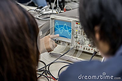 Students point Sine Wave at oscilloscope Stock Photo