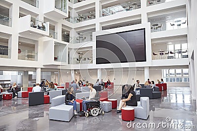 Students socialising under AV screen in atrium at university Stock Photo