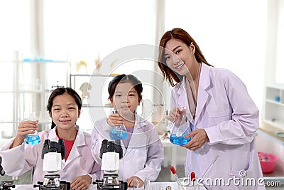 Students and teacher in lab coat have fun together while learn science experiment in laboratory. Young pretty Asian scientist and Stock Photo