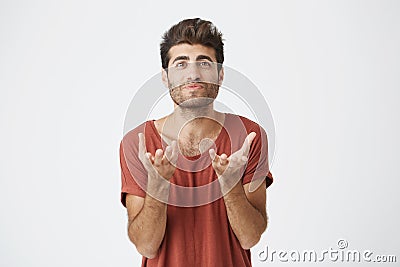 Studio portrait of attractive bearded student in red t-shirt stretching his hands to the camera. Emotional man with Stock Photo