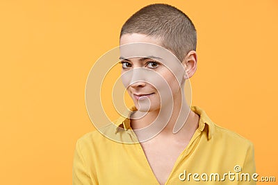 Studio portrait of a beautiful young caucasian woman with shaved head against bright yellow background. Cancer survivor portrait. Stock Photo