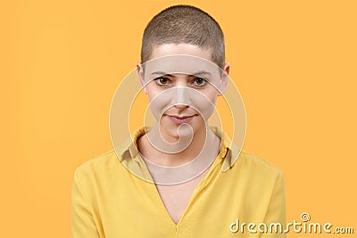 Studio portrait of a beautiful young caucasian woman with shaved head against bright yellow background. Cancer survivor portrait. Stock Photo